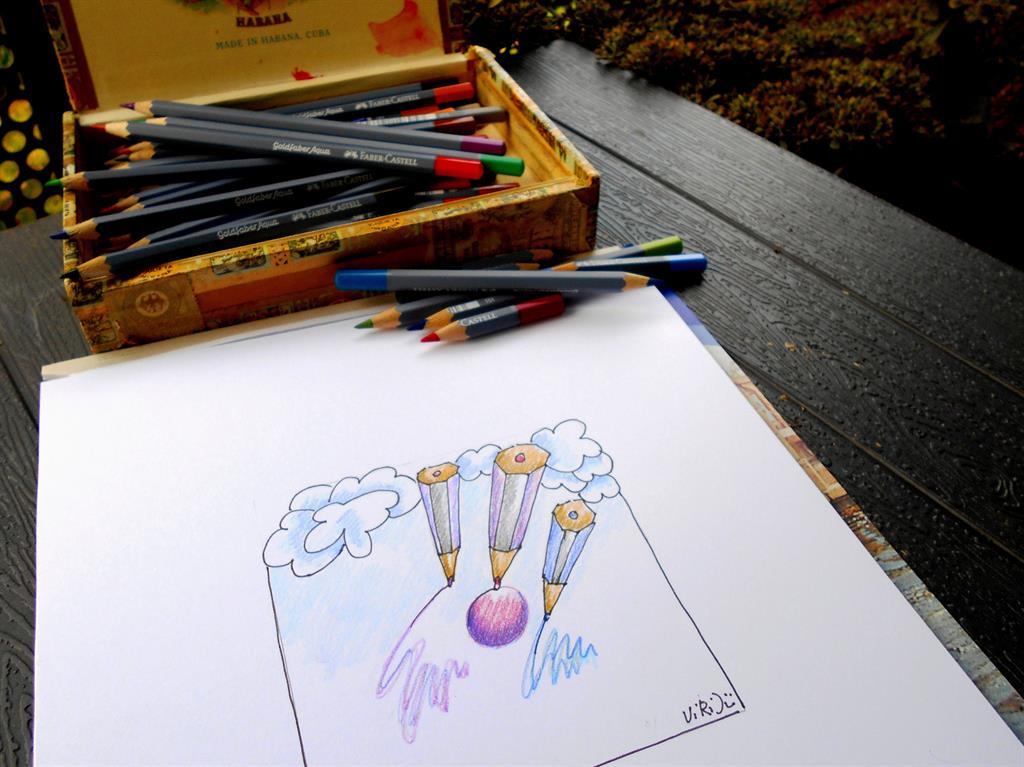 Zigarrenkiste mit Buntstiften, davor Zeichenblock mit Skizze